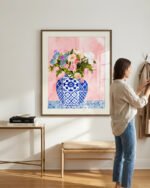An front mockup view of the attached framed art bigger yet exactly to-scale & minimally framed with a mount - on a pearl white wall, in a sunlit, fashionable, uncluttered, real, lived-in entryway - with eclectic furniture and a stylishly minimal decor. No big plants. No other wall art. A person is casually present in the room. The frame has a glass cover with a reflection. The focus is the vibe of the space.